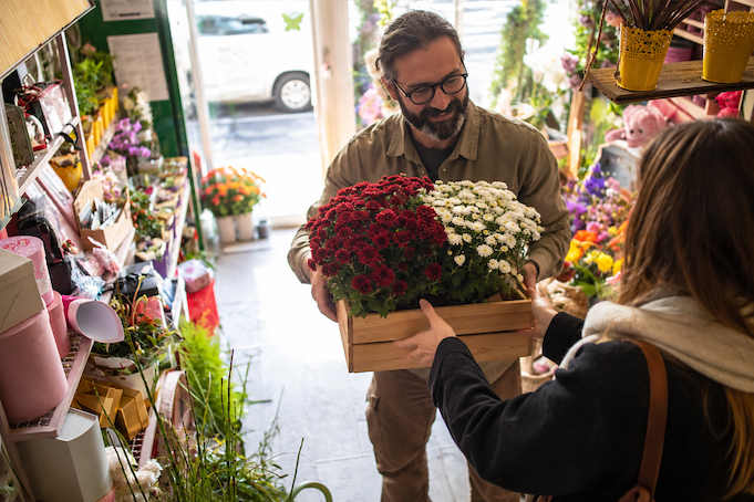 Un fleuriste remet une caisse de chrysanthèmes rouges et blancs à une cliente au marché