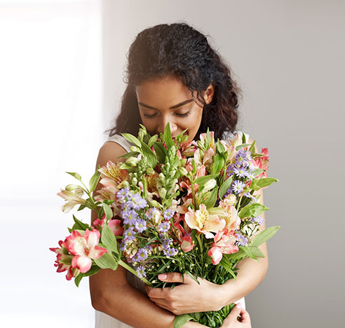Femme respirant un bouquet de fleurs de saison livré par Sens Fleuriste Caviste